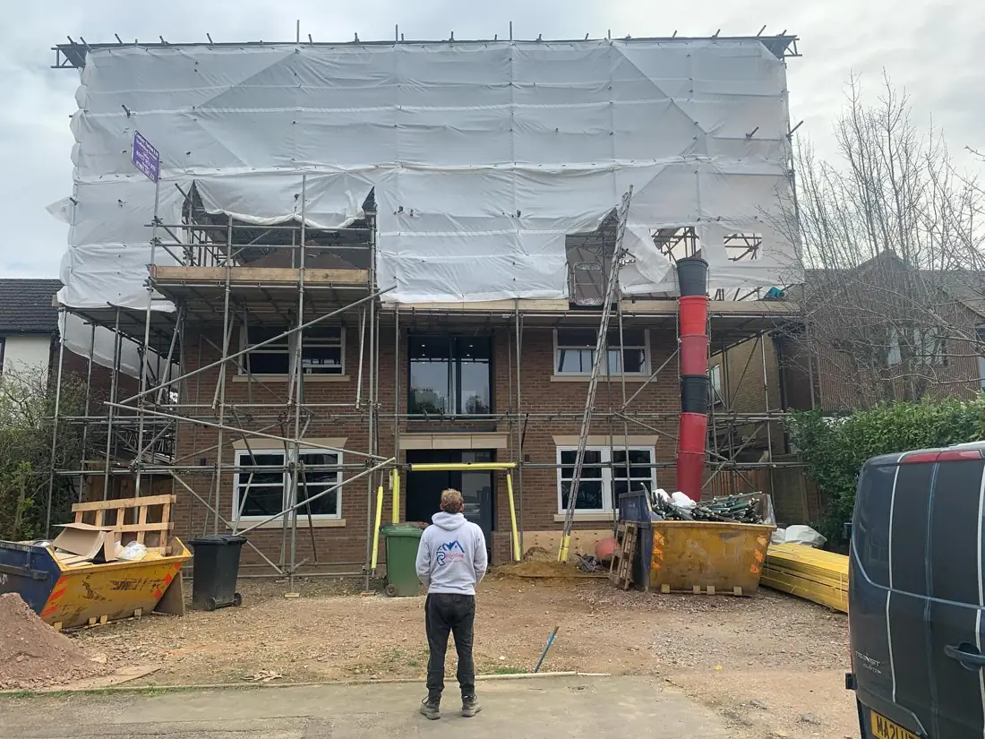 Roofer standing in front of a scaffolded house during a re-roof in Essex